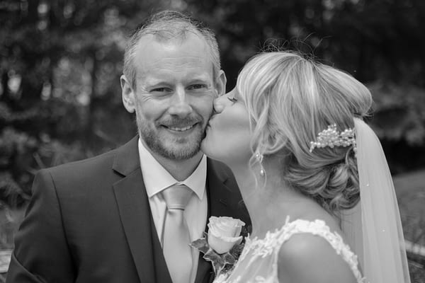 Bride kissing groom on cheek at Coltsford Mill, Oxted