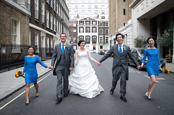Bride, groom, bridesmaids and best man walking hand in hand down London street